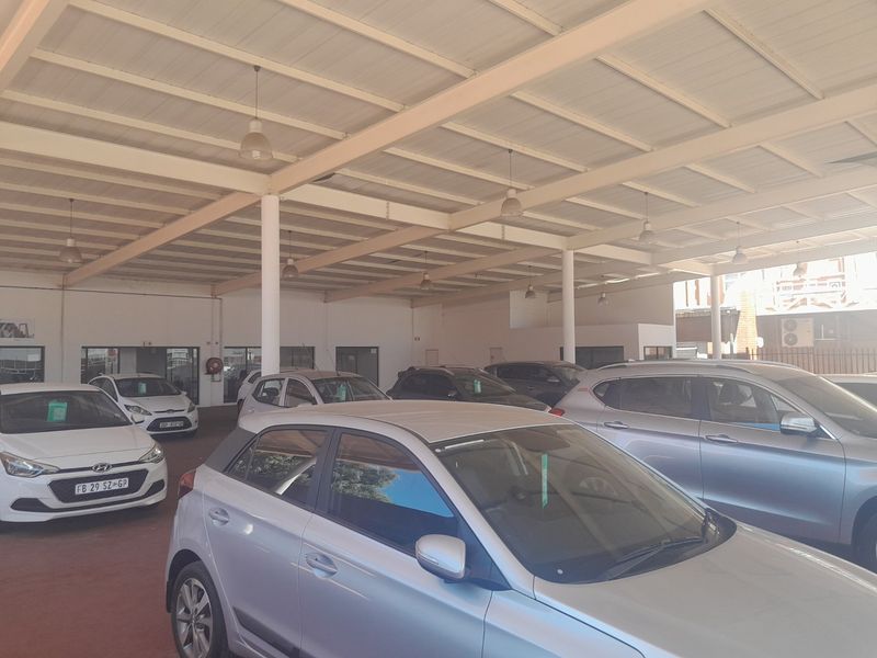 A spacious commercial garage or showroom area featuring a high steel roof structure, industrial pendant lighting, and durable concrete flooring.