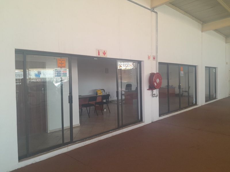 Commercial office space exterior view featuring sliding glass doors, fire safety equipment, and exposed conduit along the wall.
