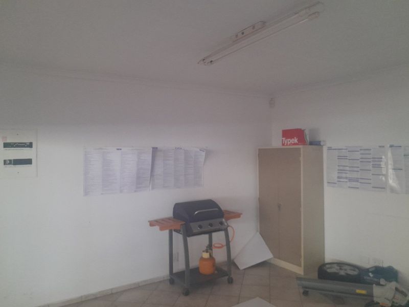 A functional utility space featuring tiled flooring, a mounted electrical distribution board, and overhead fluorescent lighting, suitable for storage or workspace requirements.