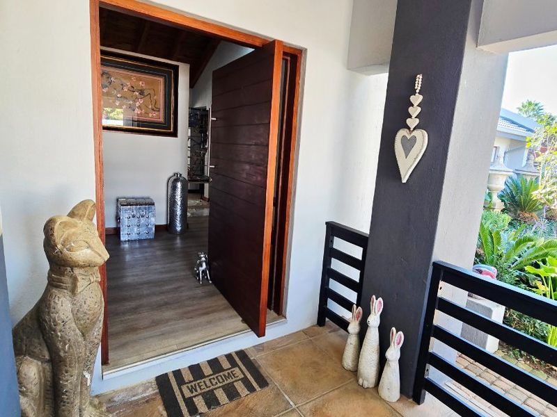 Covered entrance porch featuring tiled flooring, a modern timber pivot door, and a dark-painted structural pillar with metal balustrade detailing.