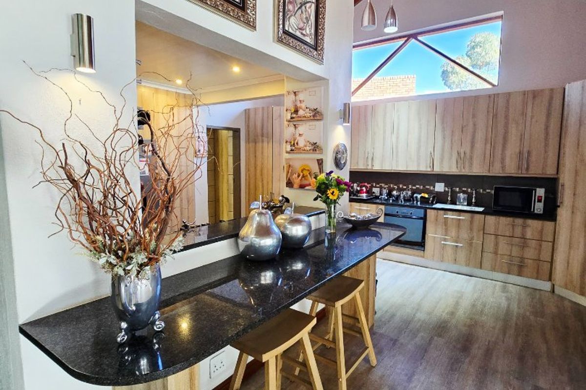 Modern kitchen featuring a granite breakfast bar, ample built-in cabinetry, and striking exposed timber ceiling beams with a unique triangular window.