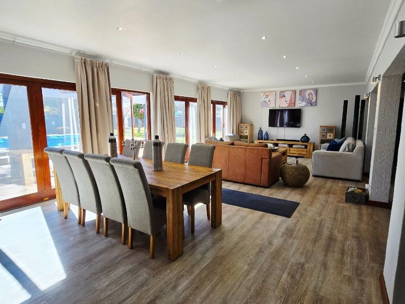 Spacious open-plan living and dining area featuring modern laminate flooring, recessed lighting, and multiple sliding glass doors providing access to the outdoor pool area.
