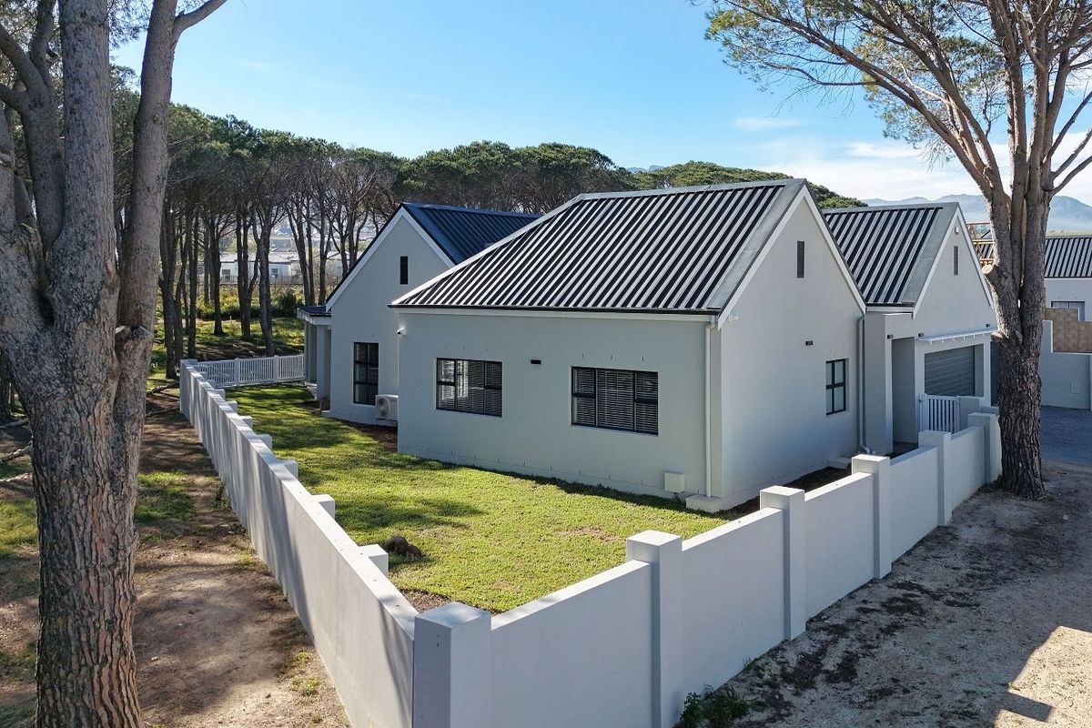 A modern house exterior featuring a metal roof, clean rendered walls, and a private garden enclosed by a perimeter wall.