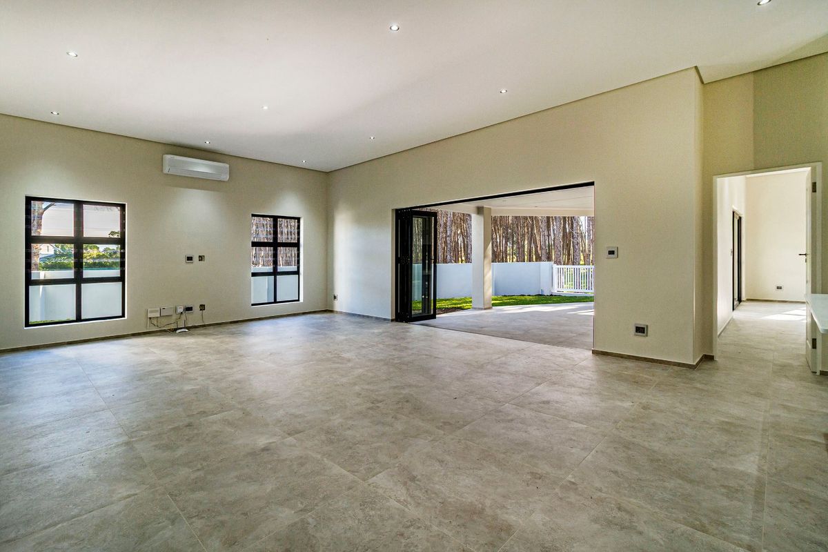 Spacious, modern open-plan living area featuring large-format floor tiles, recessed lighting, and seamless access to a covered patio through stacking doors.