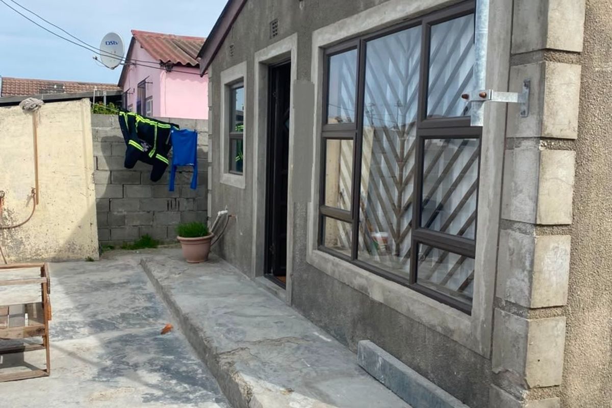 Rear exterior view of the property featuring a concrete patio area, aluminium window frames with security bars, and a cinder block boundary wall.