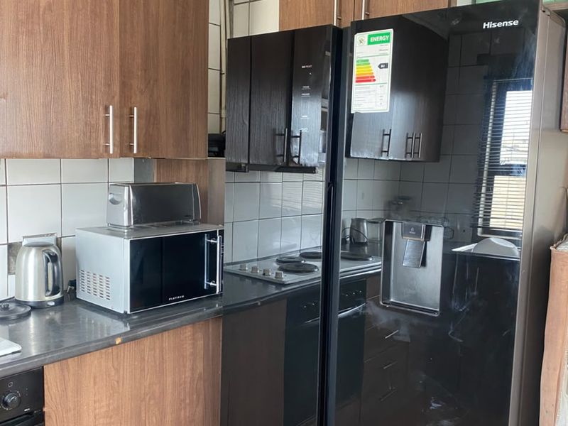 A functional kitchen featuring wood-look cabinetry, tiled backsplash, and integrated appliances, offering a practical layout with potential for modern cosmetic updates.