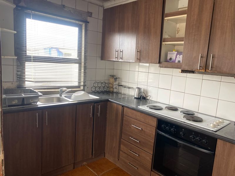 A dated kitchen featuring wood-look laminate cabinetry, a built-in oven with electric hob, and tiled finishes, requiring cosmetic updates and repairs.