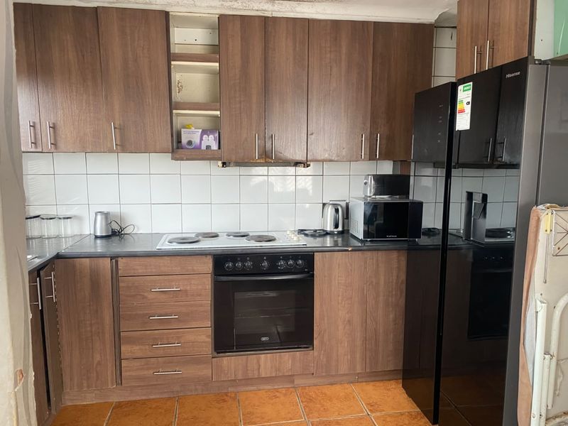 A dated kitchen featuring wood-look cabinetry, a built-in oven and hob, tiled backsplash, and ceramic flooring, requiring cosmetic updates to modernize the space.