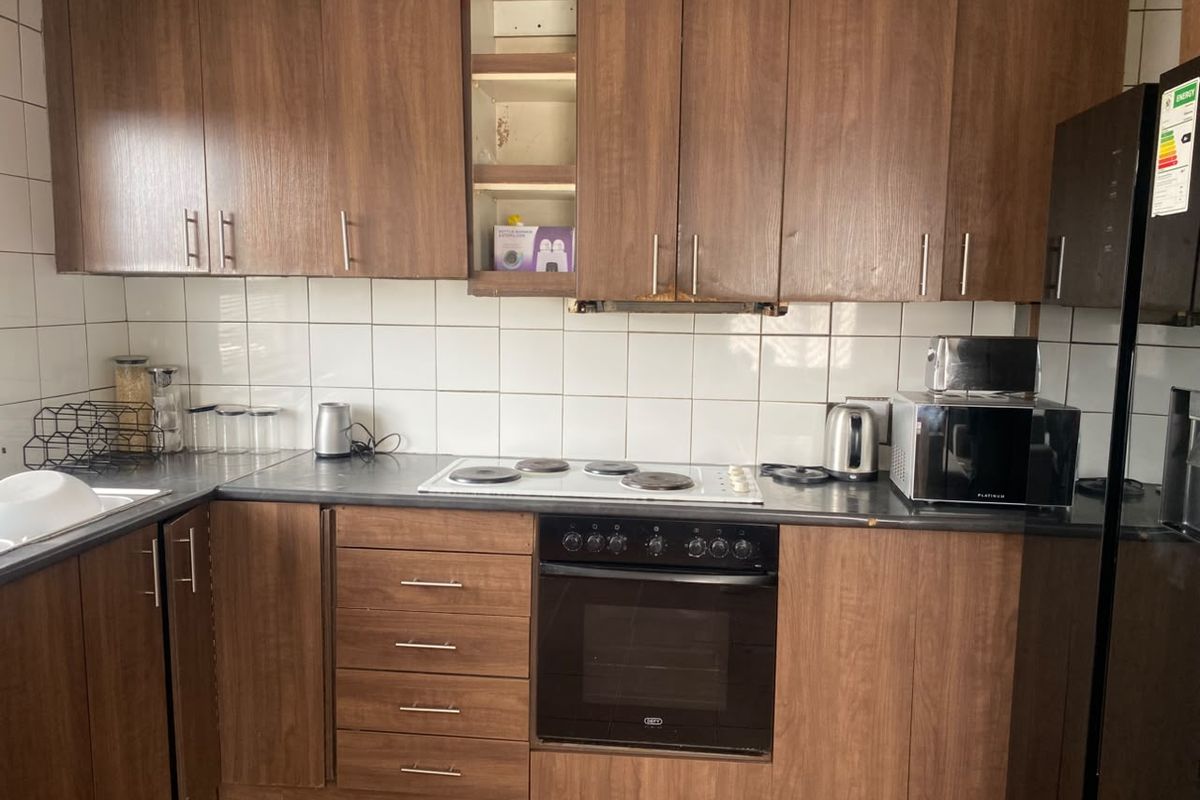 A functional kitchen featuring wood-look laminate cabinetry, a built-in oven, electric hob, and tiled backsplash, currently showing signs of wear.