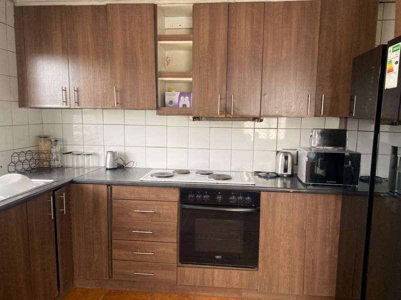 A functional kitchen featuring wood-look laminate cabinetry, a built-in oven, electric hob, and tiled backsplash, currently showing signs of wear.