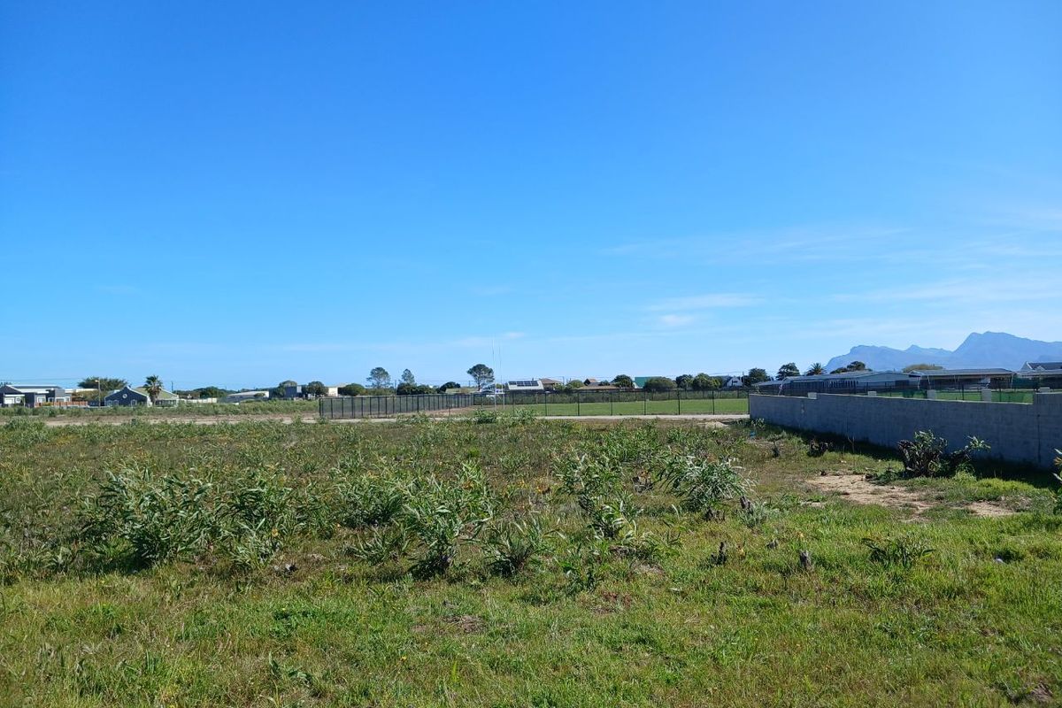A vacant residential plot featuring natural vegetation, enclosed by a perimeter wall and fencing, offering clear views of the surrounding neighborhood and distant mountains.