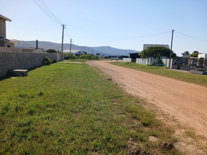 A view of the unpaved street and surrounding residential neighborhood, showing existing boundary walls and overhead utility infrastructure.