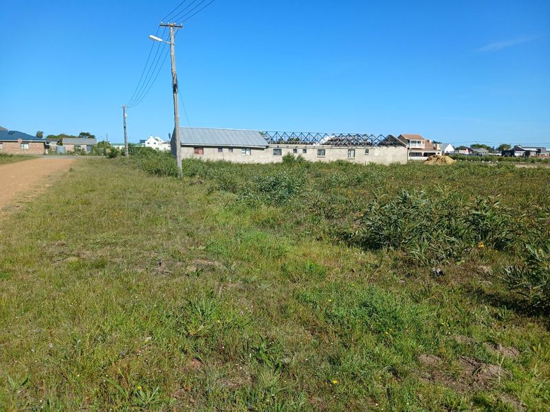 A vacant residential plot featuring native vegetation, utility connections, and a partially constructed building structure with exposed roof trusses.