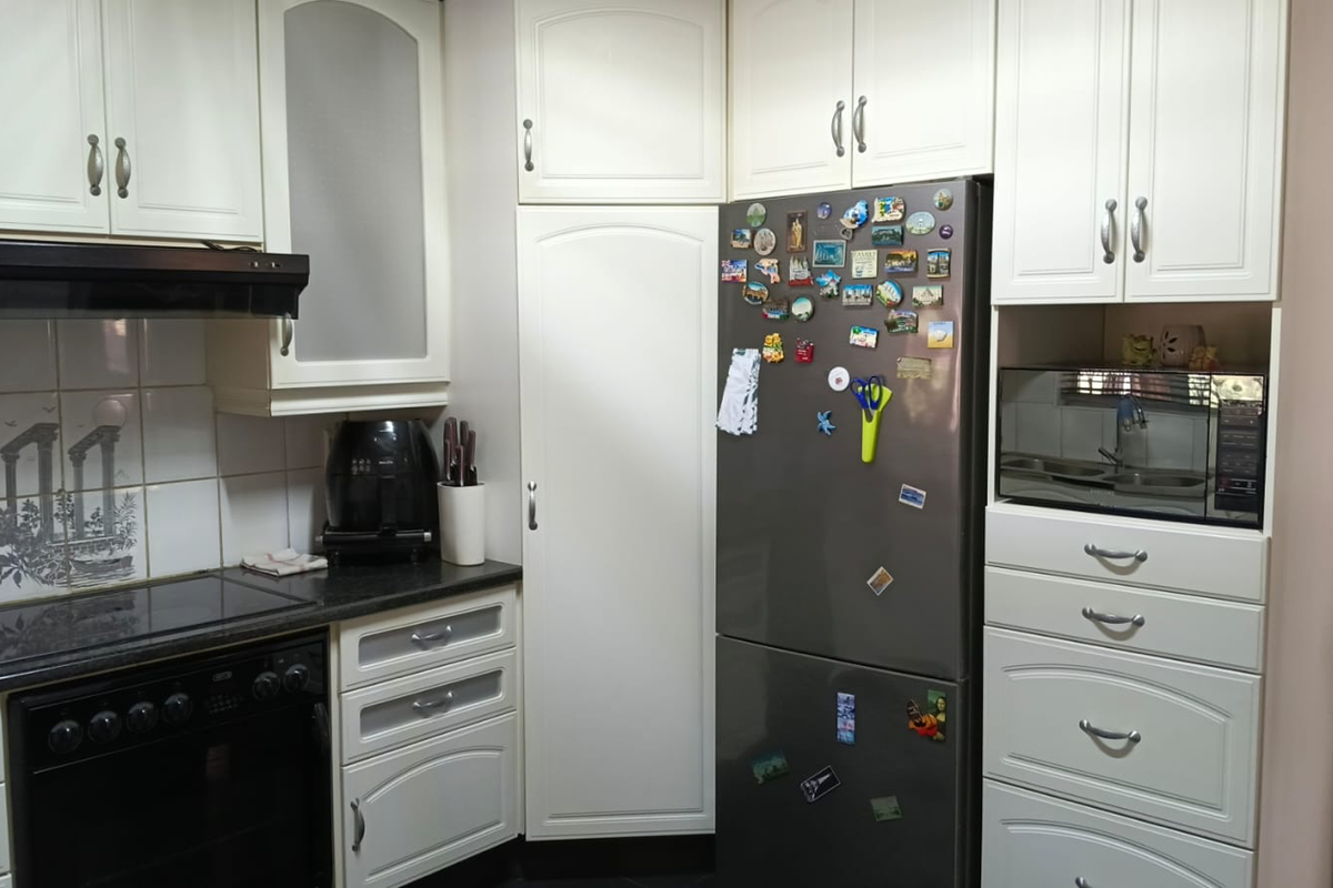 A functional kitchen featuring white cabinetry, granite countertops, a built-in oven with hob, extractor fan, and a dedicated space for a microwave.