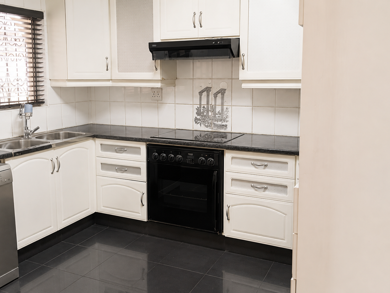 A functional kitchen featuring white cabinetry, dark granite countertops, a built-in oven with hob, and a double sink with tiled backsplash.