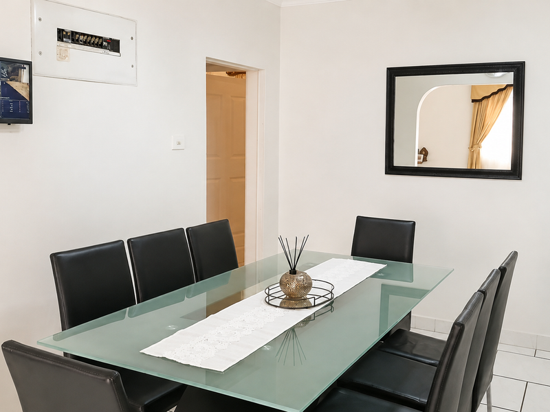 A bright dining room featuring tiled flooring and a wall-mounted electrical distribution board, providing a clean and functional space for family meals.