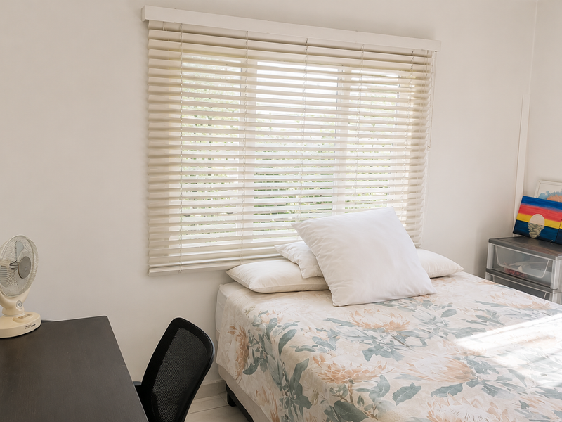 A bright bedroom featuring neutral walls and fitted venetian blinds, providing a clean and functional space.