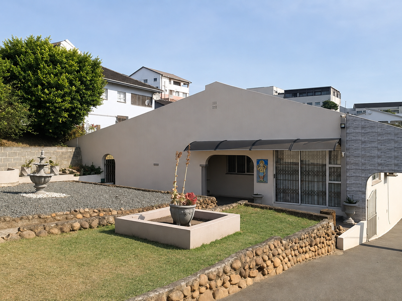 Front view of the property featuring a paved driveway, stone retaining walls, a landscaped garden with a fountain, and a covered entrance area.