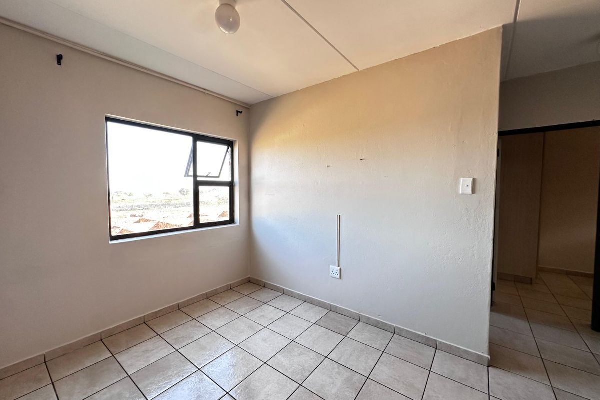 A vacant bedroom featuring neutral tiled flooring, a large aluminium-framed window, and basic electrical fixtures, ready for personalization.