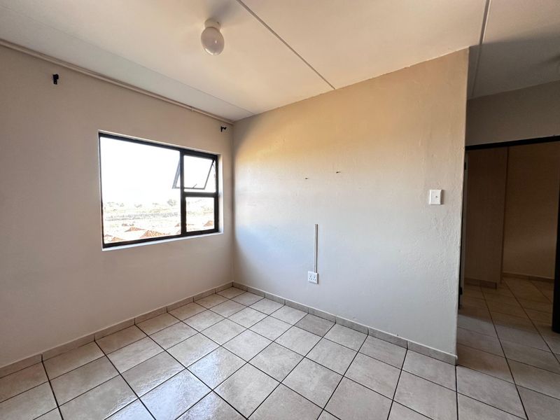 A vacant bedroom featuring neutral tiled flooring, a large aluminium-framed window, and basic electrical fixtures, ready for personalization.