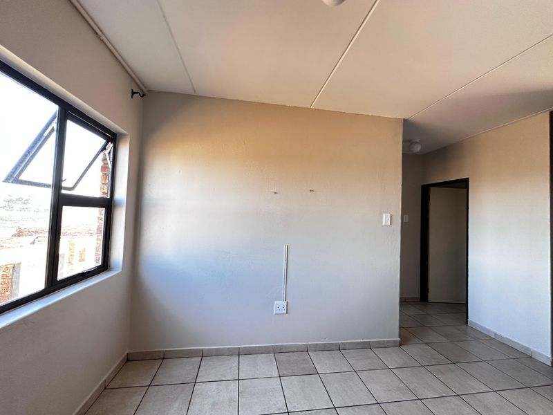 An empty bedroom featuring neutral tiled flooring, a large aluminium window, and a simple interior doorway, ready for personalization.