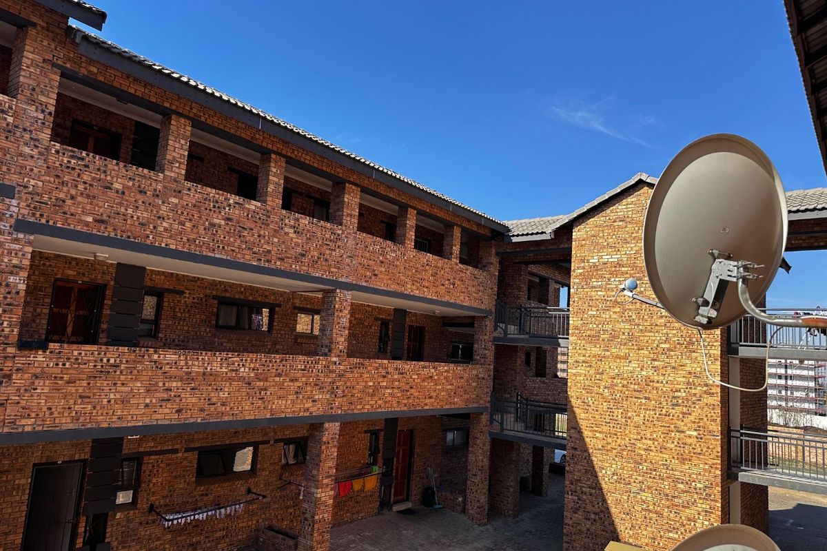 Exterior view of a multi-story apartment complex featuring face brick construction, open walkways with metal railings, and a paved central courtyard area.