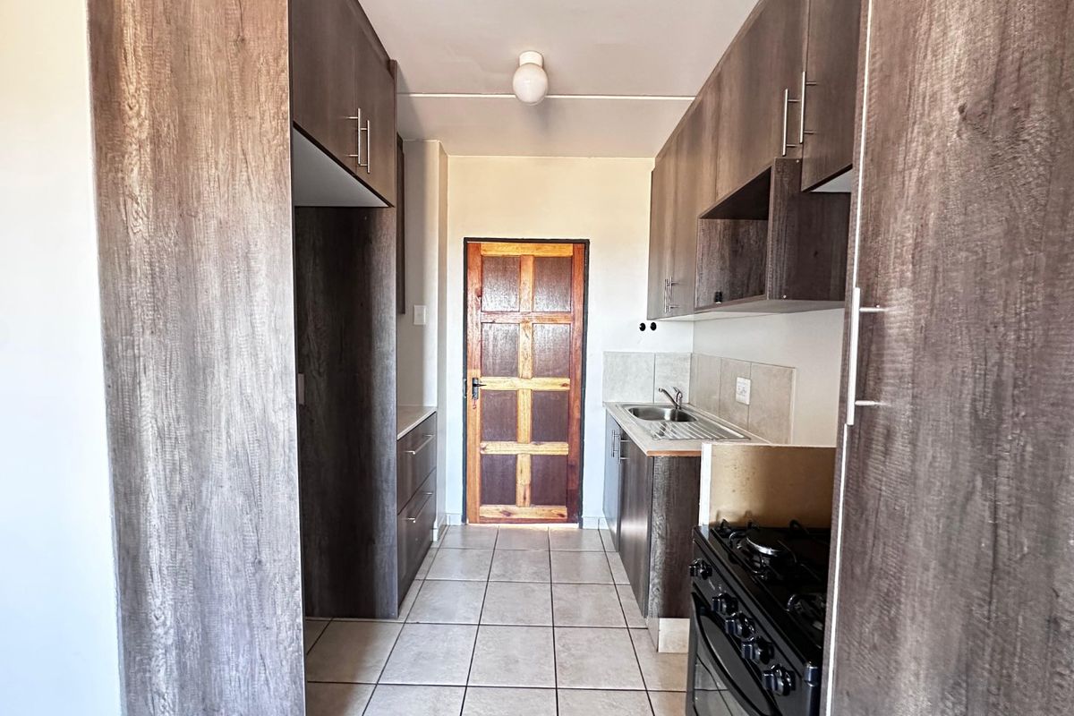 A functional galley-style kitchen featuring dark wood-look cabinetry, tiled flooring, a stainless steel sink, and a freestanding stove.