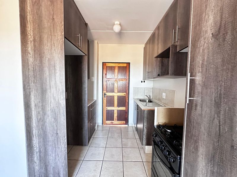 A functional galley-style kitchen featuring dark wood-look cabinetry, tiled flooring, a stainless steel sink, and a freestanding stove.