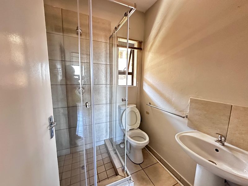 A functional bathroom featuring a glass-enclosed shower, pedestal basin, and toilet with neutral floor and wall tiling.