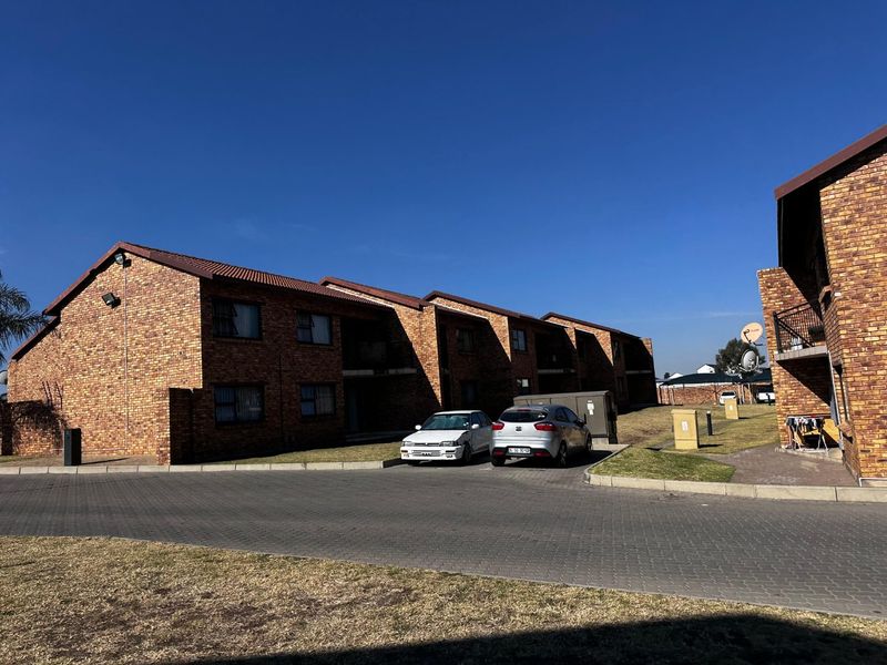 Exterior view of a multi-story face brick apartment complex with a paved driveway and landscaped grounds.