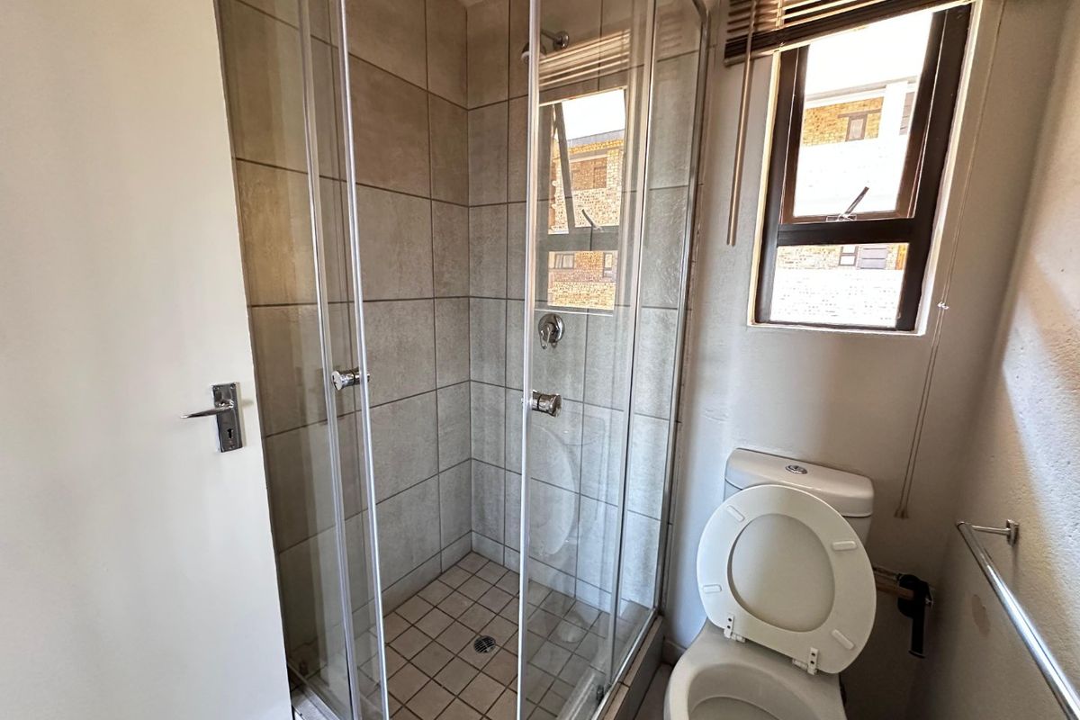 A functional bathroom featuring a glass-enclosed shower, a standard toilet, and a window for natural light.