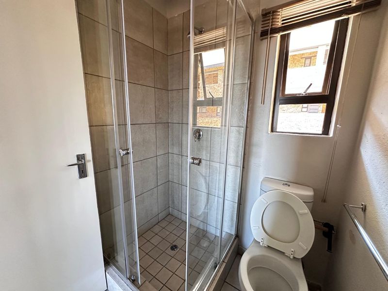 A functional bathroom featuring a glass-enclosed shower, a standard toilet, and a window for natural light.