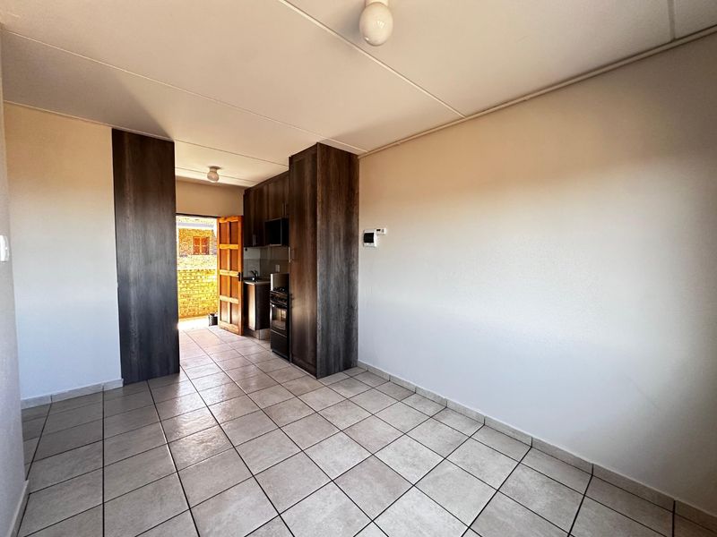 An open-plan living and kitchen area featuring tiled flooring, dark wood-finish cabinetry, and a freestanding stove, leading to an exterior doorway.