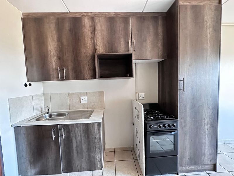 Compact kitchen featuring dark wood-look cabinetry, a stainless steel sink, tiled backsplash, and a dedicated space for a freestanding stove.
