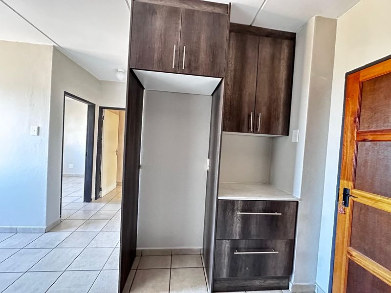 A functional kitchen area featuring dark wood-finish built-in cabinetry, a laminate countertop, and neutral tiled flooring, providing a clean and practical space.