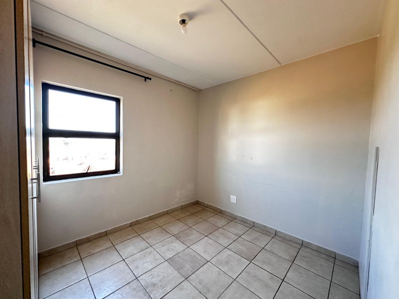 An empty bedroom featuring tiled flooring, a built-in cupboard, and an aluminium window frame, providing a blank canvas for personalization.
