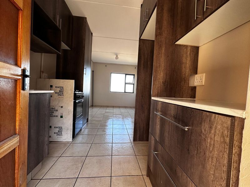 A functional kitchen area featuring dark wood-look cabinetry, tiled flooring, and a freestanding stove, leading into an open-plan living space.