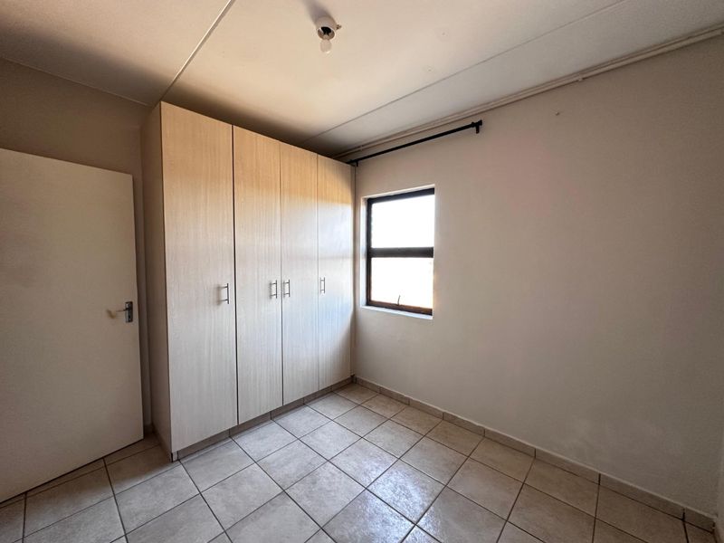 A clean, empty bedroom featuring neutral tiled flooring and built-in wooden cupboards, offering a blank canvas for personalization.