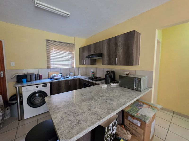 Functional kitchen featuring laminate cabinetry, stone-look countertops, built-in hob with extractor, and integrated laundry space, offering a practical layout for daily use.