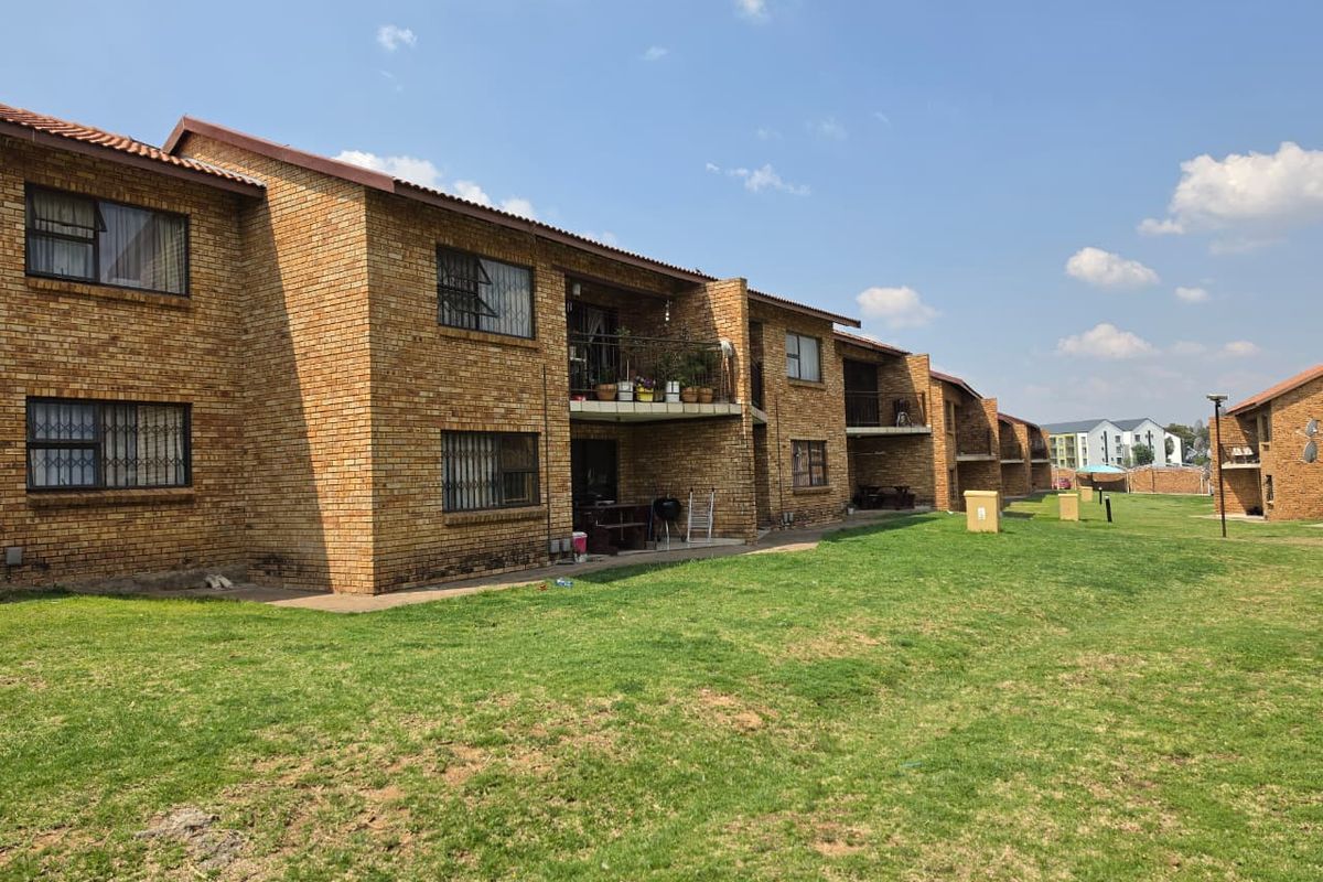 Exterior view of a multi-story apartment complex featuring face brick construction, tiled roofing, and private balconies overlooking a communal lawn area.