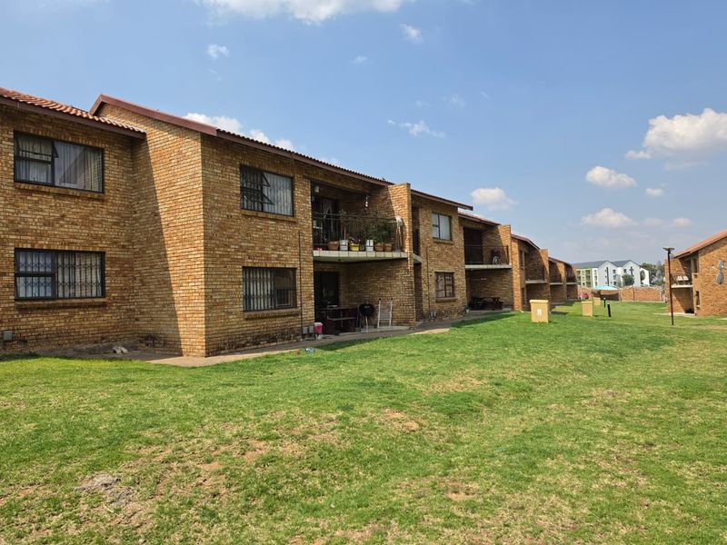Exterior view of a multi-story apartment complex featuring face brick construction, tiled roofing, and private balconies overlooking a communal lawn area.