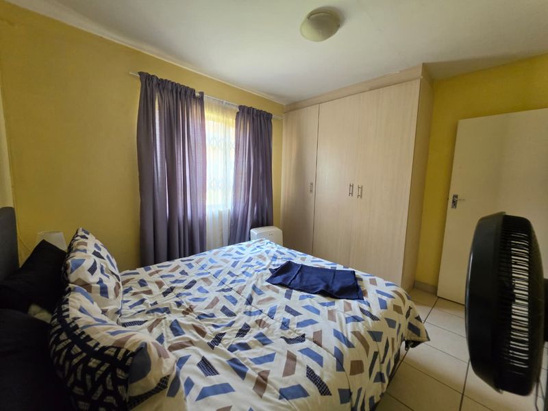 A functional bedroom featuring tiled flooring, a built-in wardrobe, and a window with security gate protection.