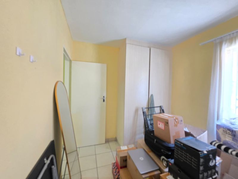 A bedroom featuring tiled flooring and a built-in wardrobe, currently used for storage.