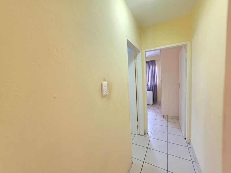 A narrow interior hallway featuring tiled flooring and yellow painted walls, providing access to adjacent rooms.