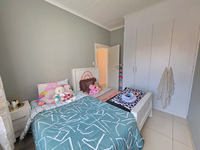 A well-maintained bedroom featuring neutral wall tones, built-in floor-to-ceiling cupboards, and clean tiled flooring.
