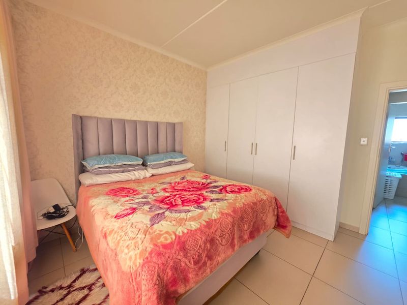 A well-maintained bedroom featuring neutral tiled flooring, built-in white cupboards, and a textured feature wall.