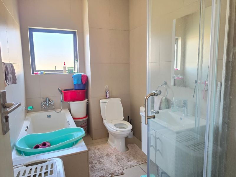 A functional bathroom featuring a built-in bathtub, a separate glass-enclosed shower, a vanity basin, and neutral wall tiling.