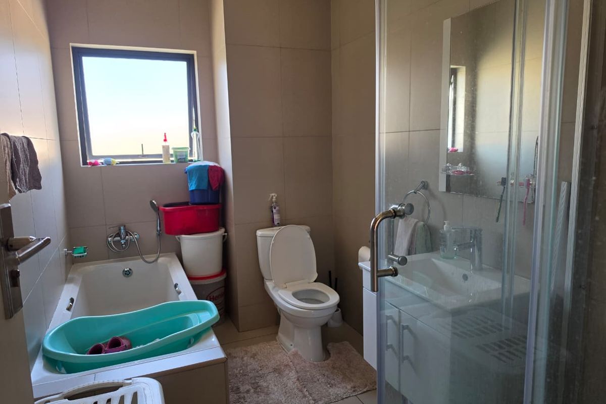 A functional bathroom featuring a built-in bathtub, separate shower enclosure, vanity cabinet with basin, and neutral wall tiling.