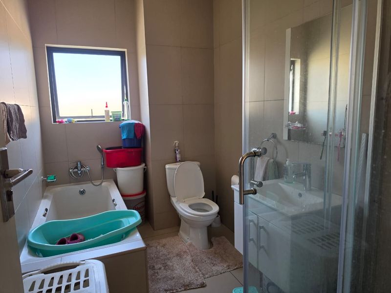 A functional bathroom featuring a built-in bathtub, separate shower enclosure, vanity cabinet with basin, and neutral wall tiling.