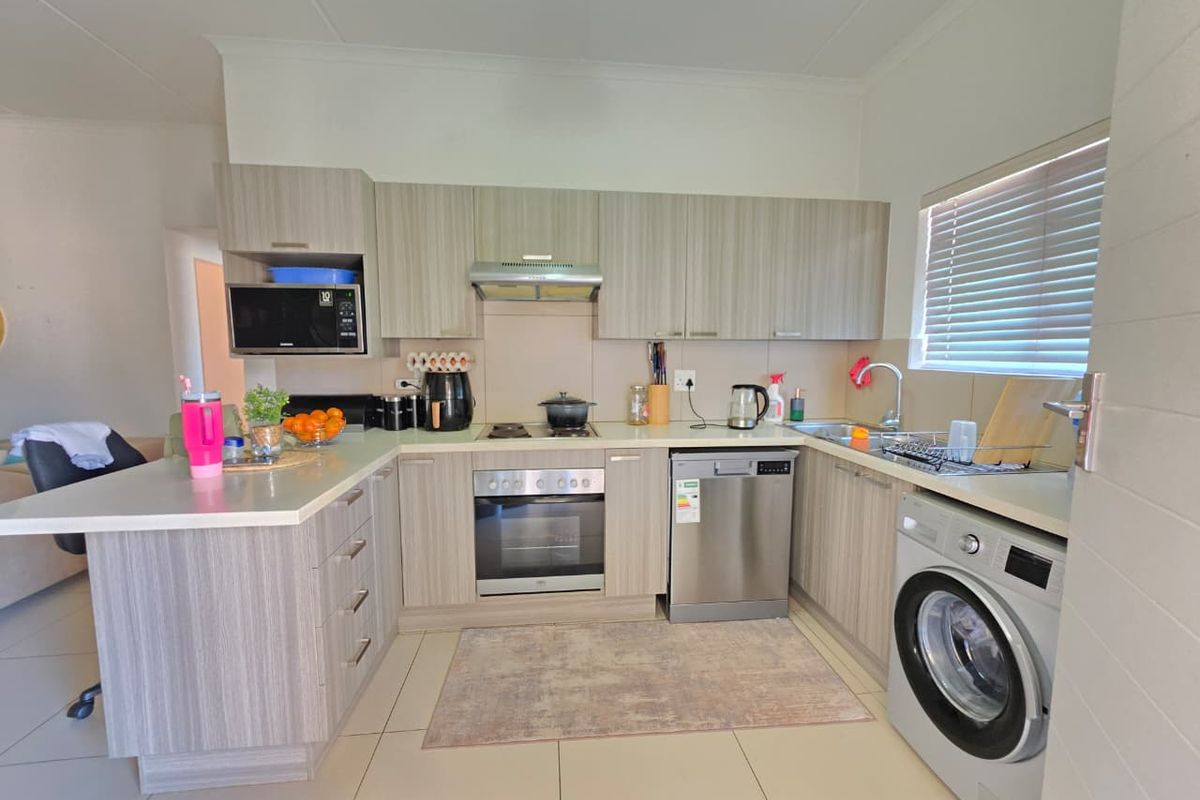 Modern kitchen featuring light wood-grain cabinetry, built-in oven, hob, extractor fan, integrated dishwasher, and tiled flooring with a functional layout.
